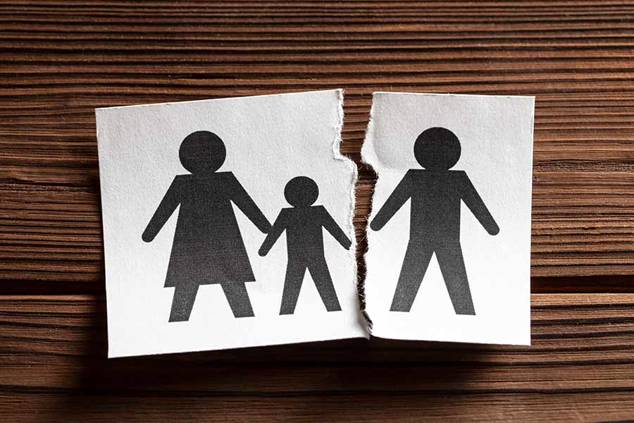 Auf braunem Holz liegt ein weisses Papier mit schwarzen Figuren bedruckt, die Vater, Mutter, Kind symbolisieren. Das Papier ist so durchgerissen, dass ein Elternteil abgetrennt ist