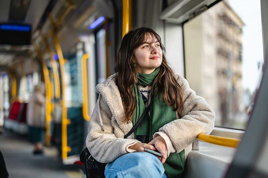 Coaching für Jugendliche und Erwachsene in Bern und Umgebung Eien Mädchen zwischen 15 - 18 Jahren sitzt in einem öffentlichen Verkehrsmittel und schaut lächelnd aus dem Fenster