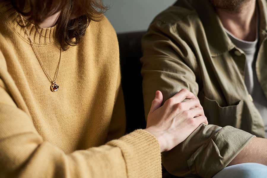 Eltern- & Paarberatung in Bern und Umgebung Eine Frau und ein Mann sitzen nebeneinander, es sind nur die angeschnittenen Oberkörper sichtbar, die Frau legt ihre Hand auf den Arm des Mannes